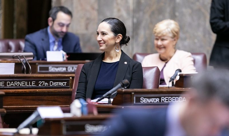 Sen Saldaña seated on the Senate floor. In the background are Sen. Keiser and Sen. Palumbo