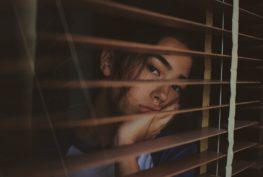 Woman looking out a window through blinds.