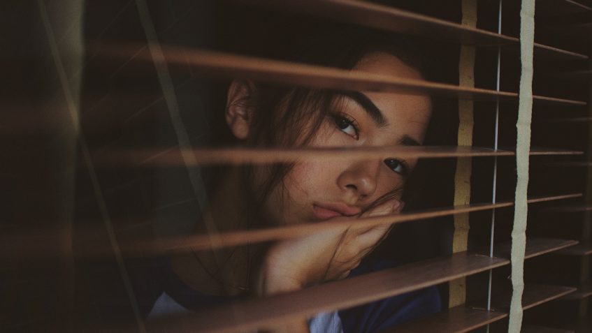 Woman looking out a window through blinds.