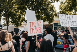 Diverse crowd protesting on the street. Protest signs say, "time for change" and "silence is violence."