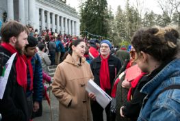 Sen. Rebecca Saldaña speaks with a a group of people standing outside the State Capitol building, and a large crowd is gathered behind them on the building's steps.