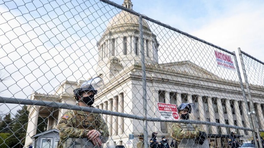 Members of the Washington National Guard and the Washington State Patrol stand guard at the perimeter fence erected around the state Capitol in Olympia on Sunday, the day before the start of the legislative session. (Bettina Hansen / The Seattle Times)