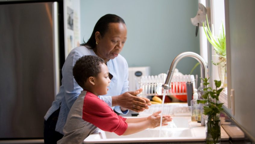 Woman and child standing at a kitchen sink washing hands.