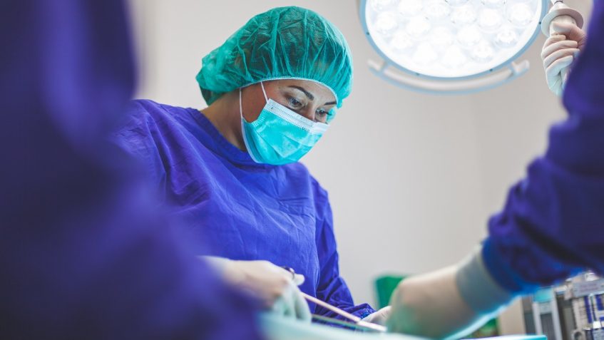 Doctor holding clamps performing procedure on unseen patient. Two people are assisting her.