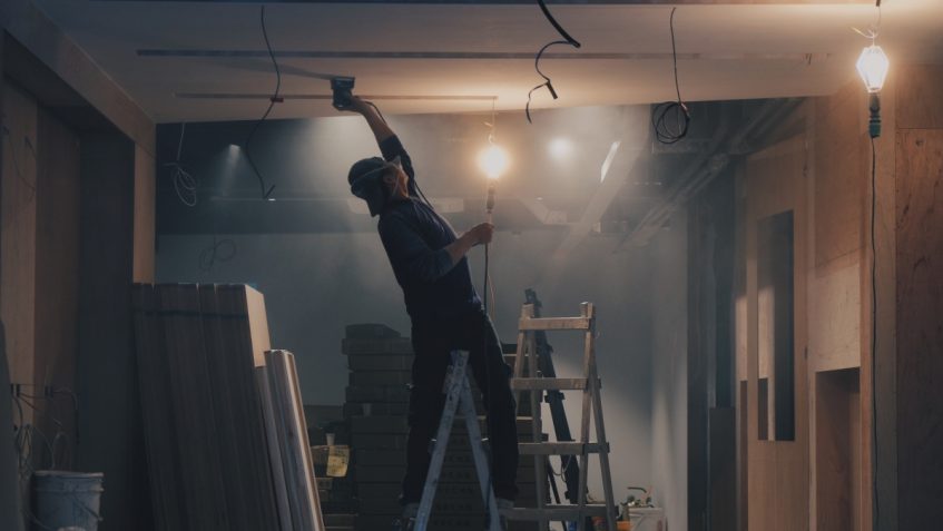 Man standing on ladder working on the ceiling in a room under construction.