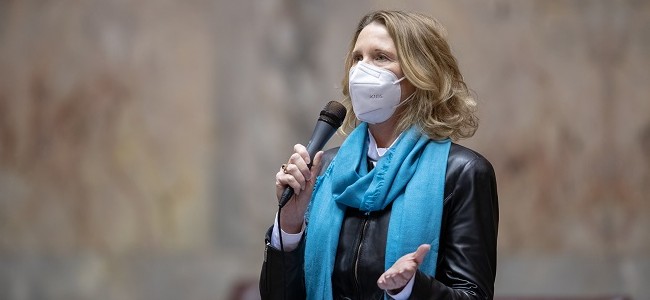Senator Patty Kuder holds a microphone and wears an N95 face mask while speaking on the floor of the state senate in Olympia